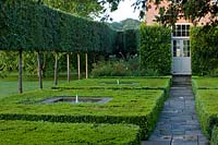 View of clipped Buxus squares with central water feature, and pleached stilt hedging.
