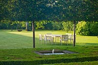 Fountain in clipped Box squares - Holm Oak stilt hedge and table and chairs