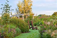 Seats surrounded with mixed borders of perennials and grasses at Frank Hejligens garden, Netherlands. 