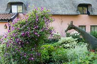 A giraffe wire mesh sculpture, made by Karen Roseberry, sits among shrubs in garden by cottage. 