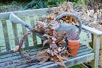 Frosty watering can with natural wreath of dried seedheads, beech leaves and ferns on garden bench