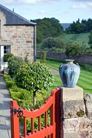View of bronze urn on gatepost and red garden gate. 