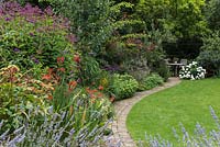 Packed herbaceous border with curved path leading to seating area. Plants include:
 of Lavandula - lavender, Eupatorium and Crocosmia