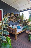 Balinese style daybed on a front verandah in front of a wall display of hexagonal timber planters. 