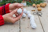 Close up detail of person threading walnuts using a piece of floristry wire. 