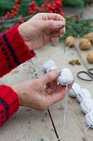 Close up detail of person threading walnuts using a piece of floristry wire. 