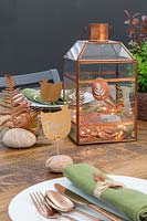 Copper themed Easter display in lantern with chicken shaped name cards fixed to pebbles with copper wire