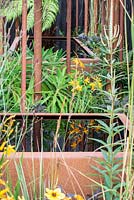 Reflection of Crocosmia 'George Davison' in a Corten water container - Bee's Gardens: The Penumbra, RHS Tatton Park Flower Show 2018