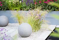Stipa tenuissima and Verbena bonariensis 'Lollipop' planted in the gravel by 
water and stone globe lights