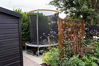 London garden designed by Nick Gough 
Wooden trellis with Verbena bonariensis screening children's play area with 
trampoline
