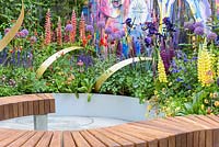 Curved iroko bench surrounded by mixed planting with yellow Lupinus 'Desert Sun' - The Supershoes, Laced With Hope Garden - RHS Chelsea Flower Show, 2018 - Sponsor: Frosts Garden Centres