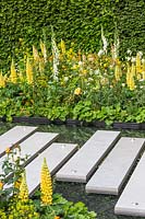 Paved stepping stones over a pebble filled pool with bright planting. The LG Eco-City Garden, Sponsor LG Electronics, RHS Chelsea Flower Show, 2018.