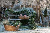A snowy bench decorated with a fir garland and baskets with greenery and candles