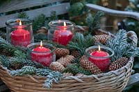 A snowy bench decorated with a fir garland and baskets with greenery and candles