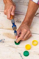 Using a hammer and nail to create a drainage hole in the bottle lid