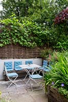 Willow hurdle fencing with Vitis vinifera around seating on North London patio.