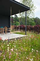 Pavilion with swing and meadow of Achillea, Lychnis and ox-eye daisy with Carpinus betulus hedge. 'A Family Garden' 