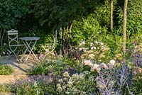 Rosa 'Wildeve', Centranthus and Salvia with table and chairs. 'Best of Both Worlds', RHS Hampton Flower Show 2018