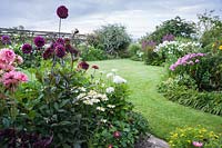 View of curved, flowering borders surrounding mown lawn. Hilltop, Stour Provost, Dorset, UK. 