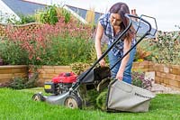 Woman emptying grass collector on petrol mower. 