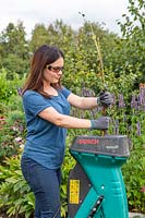 Woman using shredder to dispose of garden cuttings. 