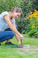 Woman using a handfork to secure the sprinkler in place on lawn