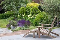 Adirondack chair on terrace with border of phormium, euphorbia, Hydrangea and Salvia