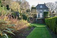 A grassy path between a box hedge and a mixed border leads towards the Orangery at Plas Brondanw, Penrhyndeudraeth, Gwynedd, Wales