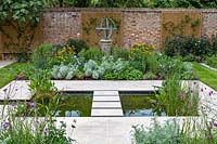 View of formal pond with rill, surrounded by mixed beds with Armillary Sundial in walled city garden. Garden design by Peter Reader Landscapes.