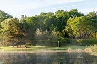 Mist rising from the lake at sunrise, with view to clipped Hornbeam hedge enclosures.