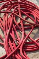 Red coiled industrial grade rubber watering hose on concrete