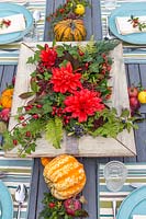 View of autumnal table setting, with floral arrangement, squashes and rose hip place settings.