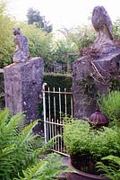 Gateposts in the form of the owl and the pussycat surrounded by lush ferns and climbing clematis at the Barn House, Glos in May