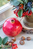 Pomegranate and hazelnuts decorate windowsill beside festive floral arrangement.