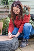 Woman marking where to make holes in base of planter to attach to tyre.