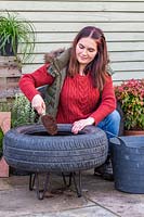 Woman adding compost into tyre container.