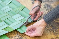 Woman trimming the excess material off woven Phormium table mat.
