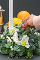Woman adding silver decorative star pick to Christmas advent candle arrangement.
