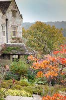 View of house through dramatic autumn shrubs and trees. Gravetye Manor, Sussex, UK. 