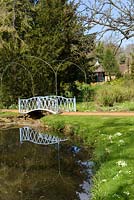 Blue metal arched bridge over pond with arch supports, trees and Indian kiosk in distance
