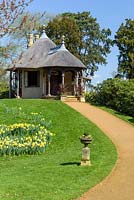 Curved path leading to the Swiss-style thatched cottage, next to lawn with daffodils
