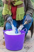 Woman washing hand trowel in bucket of soapy water.