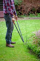 Man trimming the edge of a lawn with long handled shears.