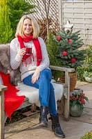 Woman sat on bench with sheepskins having a warm drink, surrounded by Christmas greenery and decorations