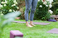 Woman standing barefoot on grass beside yoga mat. 