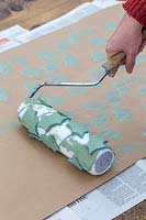 Using roller with foam patterns to create holly pattern on craft wrapping paper.