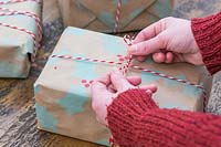 Woman tying bakers twine bow on present wrapped with handmade craft wrapping paper.