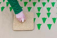 Creating continuous Christmas tree pattern onto brown wrapping paper with 
cork stamp