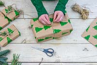 Woman tying string bow on christmas gift wrapped with hand printed wrapping paper.