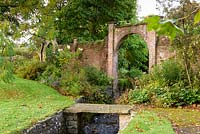 An archway in the walled Round Garden frames a stream at Llanover Gardens, Monmouthshire, UK. 